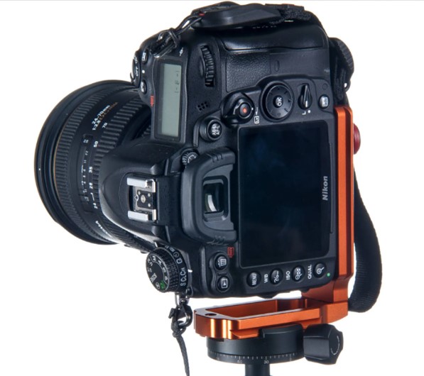 Copper coloured metal L bracket holding Nikon DSLR camera in portrait orientation on a tripod.